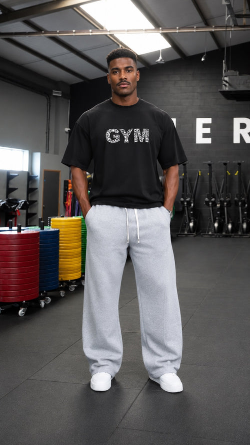 موديل يرتدي تيشيرت GYM BREAK الأسود مع بنطال رمادي واسع داخل النادي الرياضي