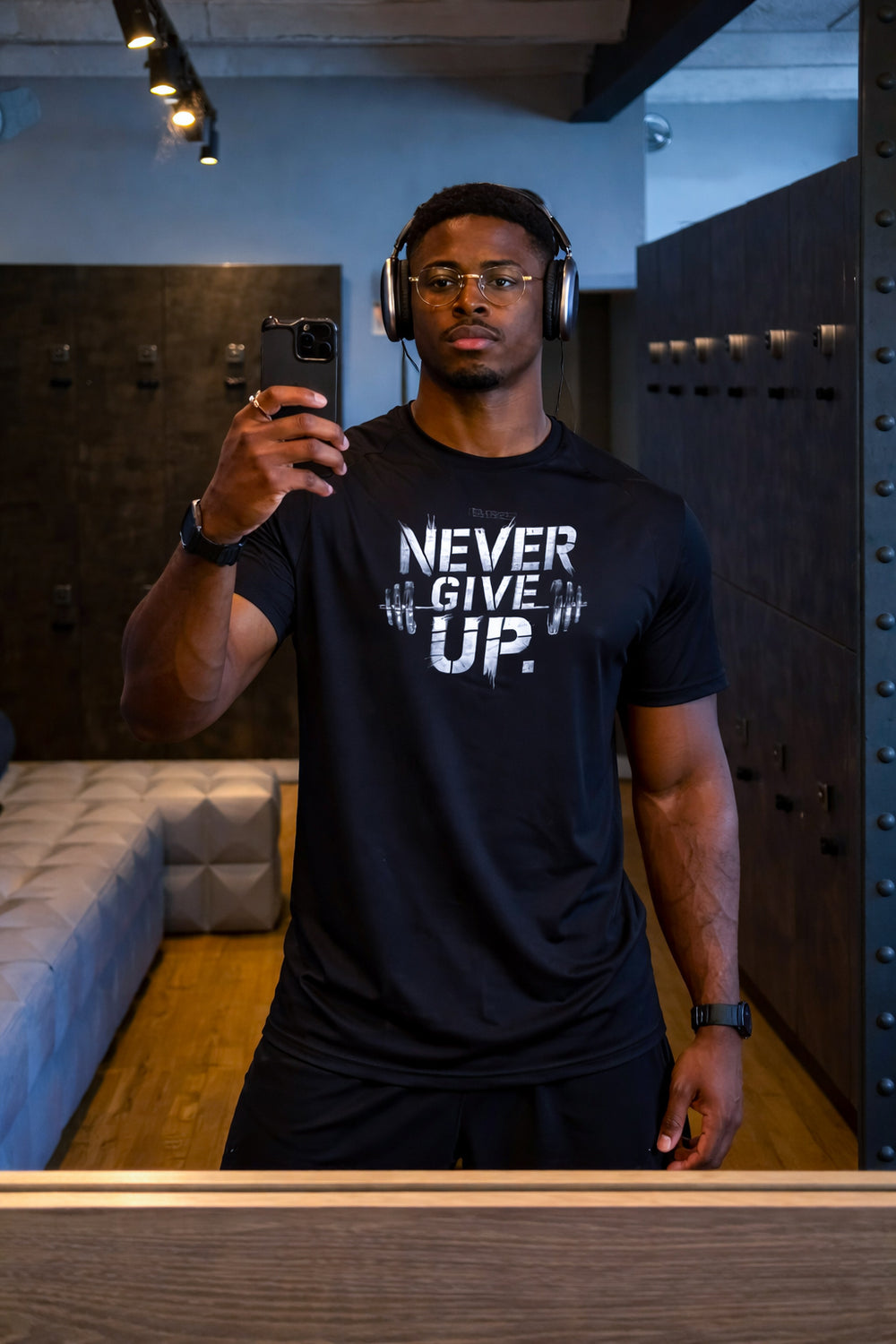 موديل يرتدي تيشيرت NEVER GIVE UP STEEL الأسود أمام المرآة داخل النادي