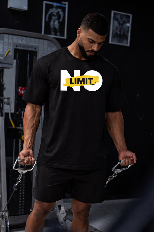 موديل يلبس تيشيرت NOVUS NO LIMIT الأسود داخل صالة جيم وهو يمسك مقابض جهاز كيبل